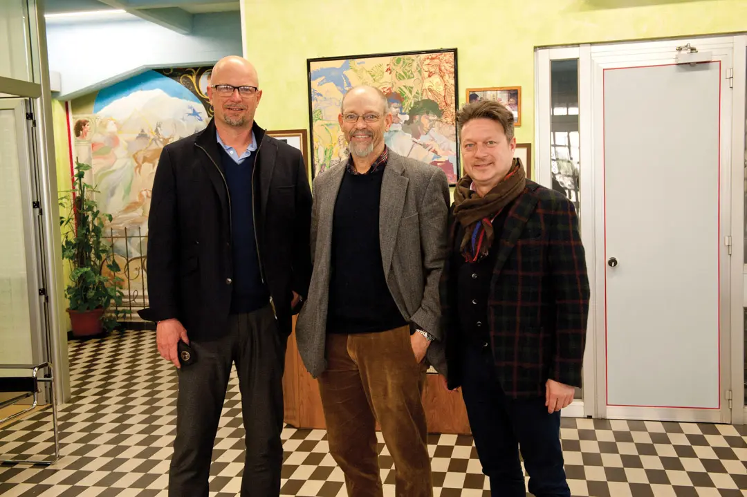 three men posing in a yellow room with a checkered floor